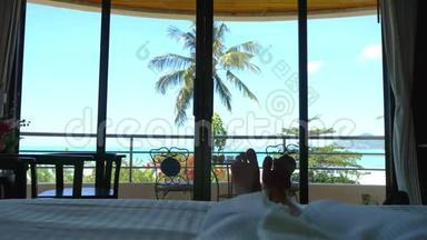穿着浴袍的女人躺在床上，挥舞着她的脚对着热带海景。 3840x2160